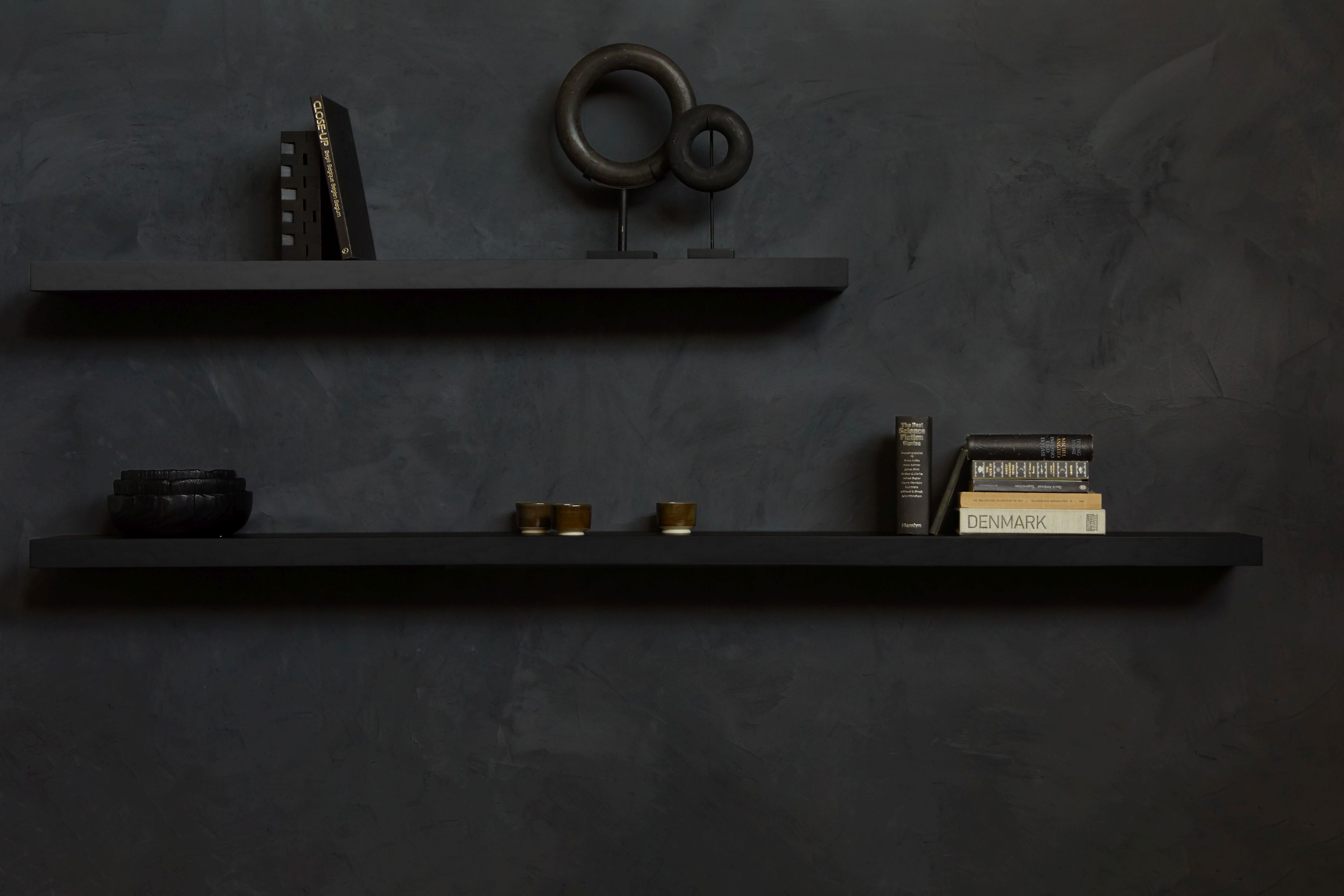 Schwarzes Ethnicraft Wandregal aus Eiche, lackiert, mit Deko-Objekten und Büchern vor einer dunklen Wand.