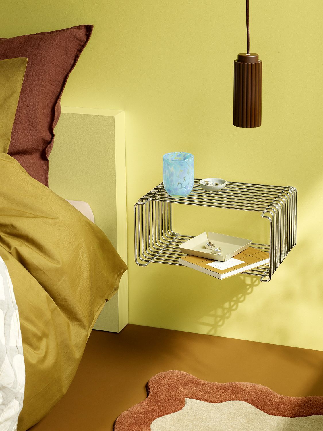 Nahaufnahme eines Panton Wire Regals als Nachttisch mit Dekoration. Chromfarbenes Wandregal.