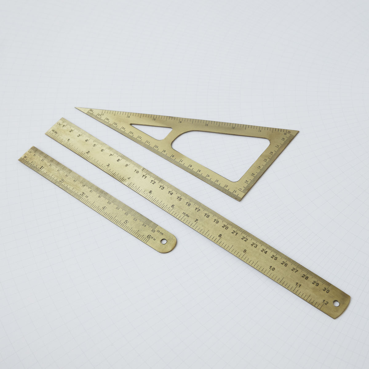 Goldfarbenes Lineal-Set mit 15 cm Lineal, Geodreieck und kurzem Lineal auf kariertem Hintergrund.