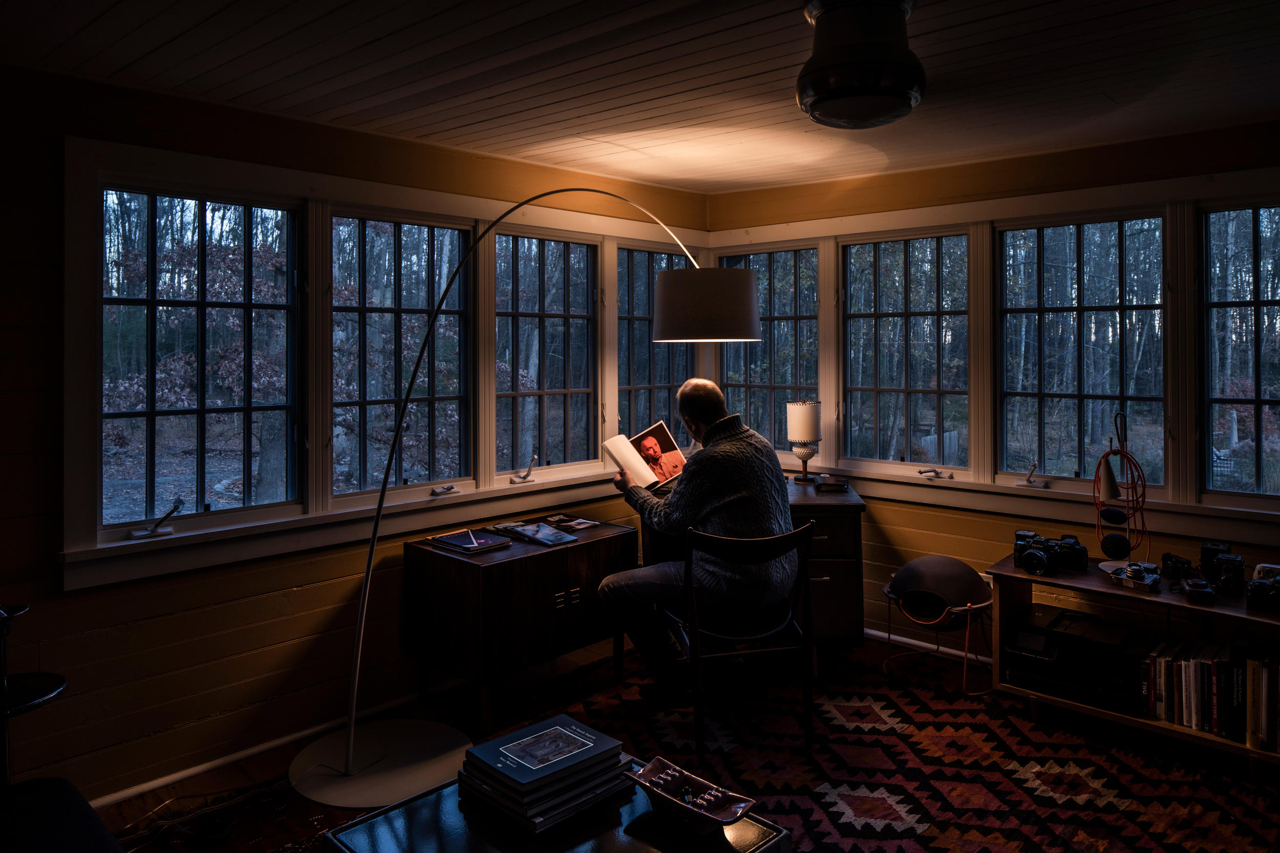Mann liest unter der grauen Foscarini Twiggy Stehleuchte in gemütlichem Wohnzimmer mit Blick auf den Wald.