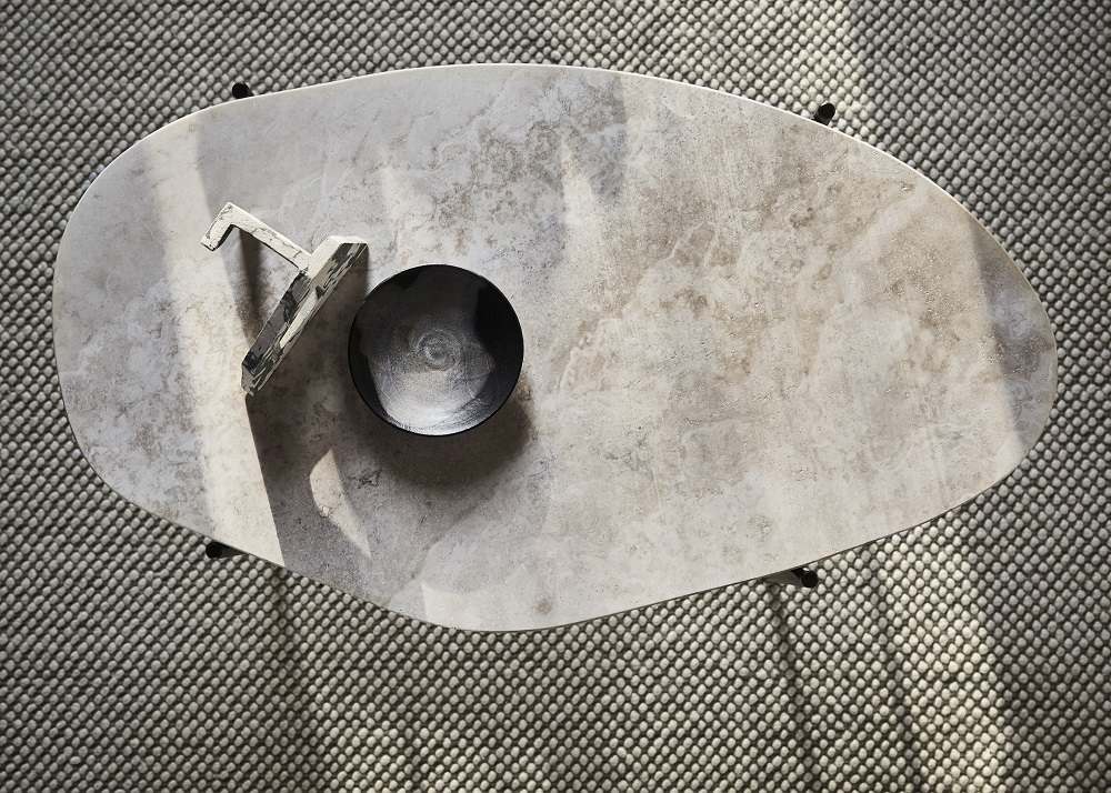 Draufsicht: La Terra Couchtisch, grau meliert, mit Deko-Objekten auf einem Teppich.