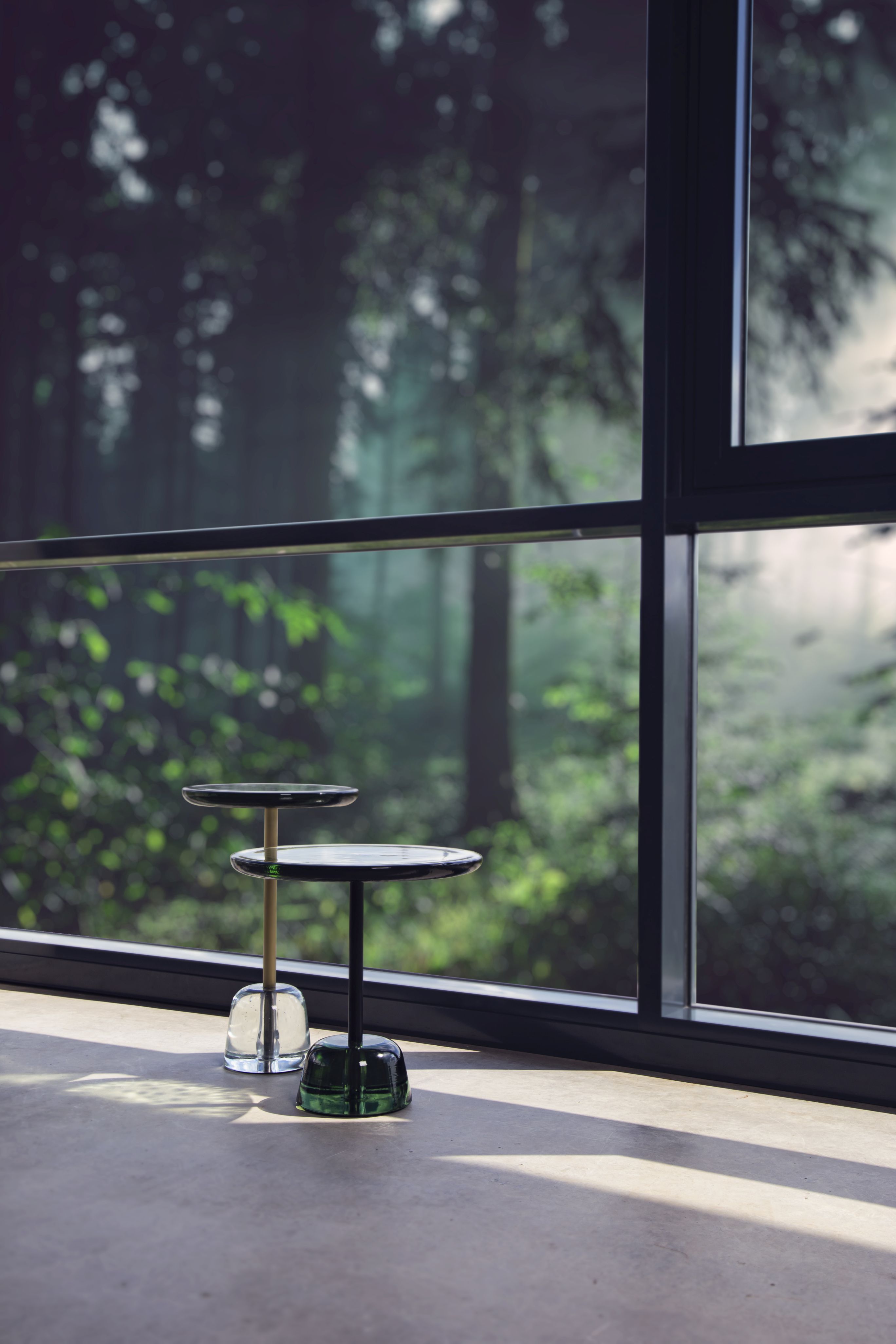 Zwei Pina High Beistelltische von Pulpo aus Glas und Metall vor Fenster.