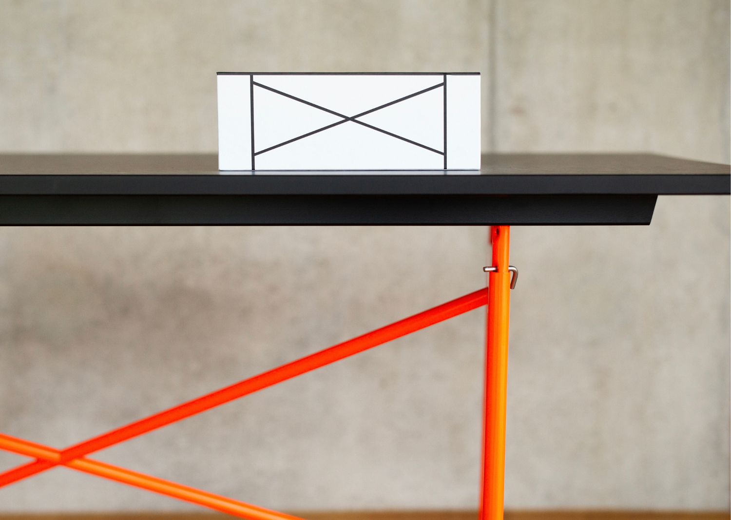 Eiermann Tisch: Detailansicht mit Musterbox, schwarzer Tischplatte und orangefarbenem Gestell. Designklassiker für Büro und Wohnen.
