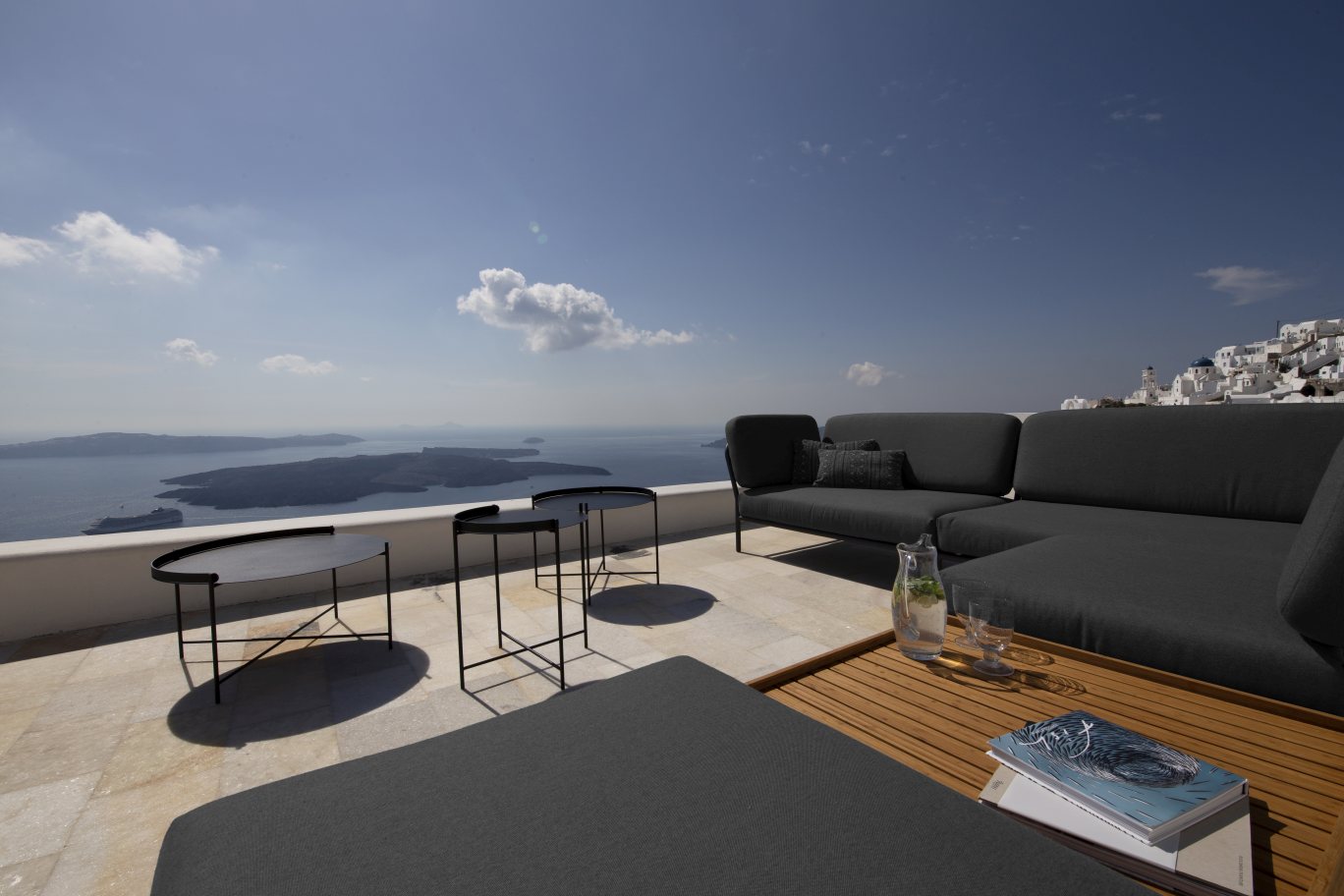 Houe Level Outdoor Sofa in Grau mit Beistelltischen auf einer Terrasse mit Meerblick.