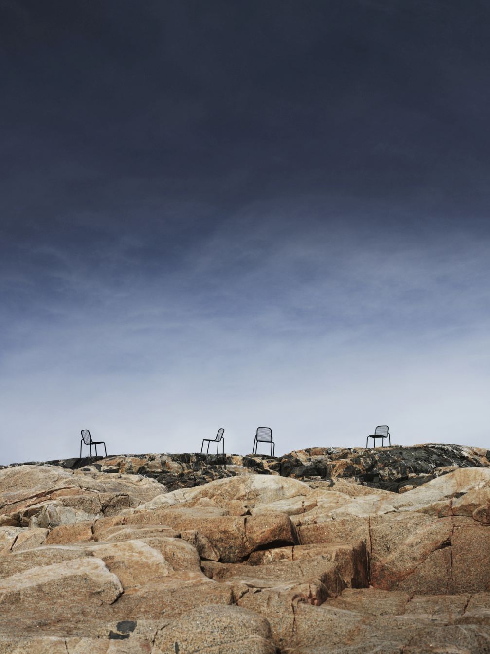 Vier Vig Chair Stühle von Normann Copenhagen stehen auf einem felsigen Untergrund im Freien.