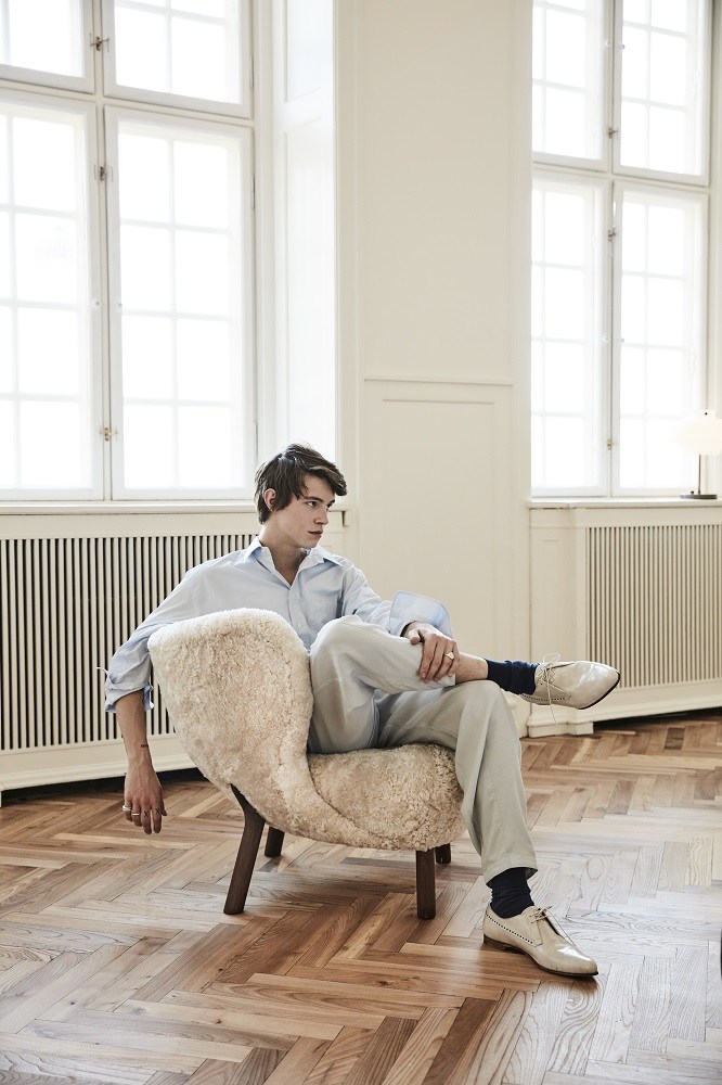 Mann entspannt im Little Petra Sessel von &Tradition, Walnussgestell, Moonlight-Bezug. Design Lounge Sessel.