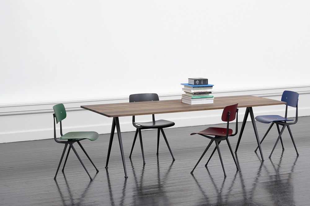 Pyramid Table 02 Esstisch von Hay mit vier farbigen Stühlen und Bücherstapel auf Tischplatte.