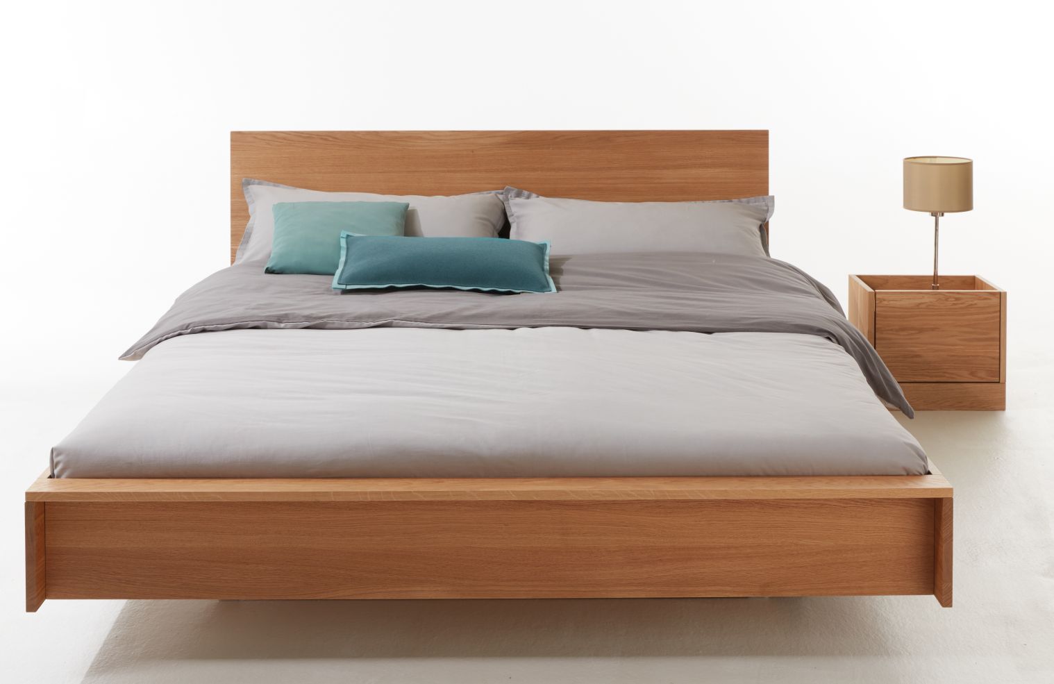 Bett mit Kopfteil aus Eiche, passender Nachttisch und Textilien in Grau und Türkis.