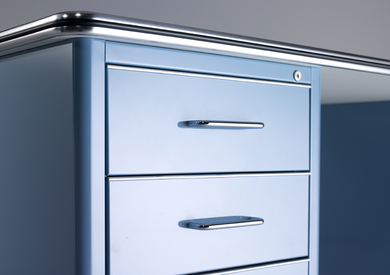 Detailaufnahme des blauen Müller Möbelfabrikation TB 225 Classic Line Schreibtischs mit drei Schubladen und Chromgriffen.