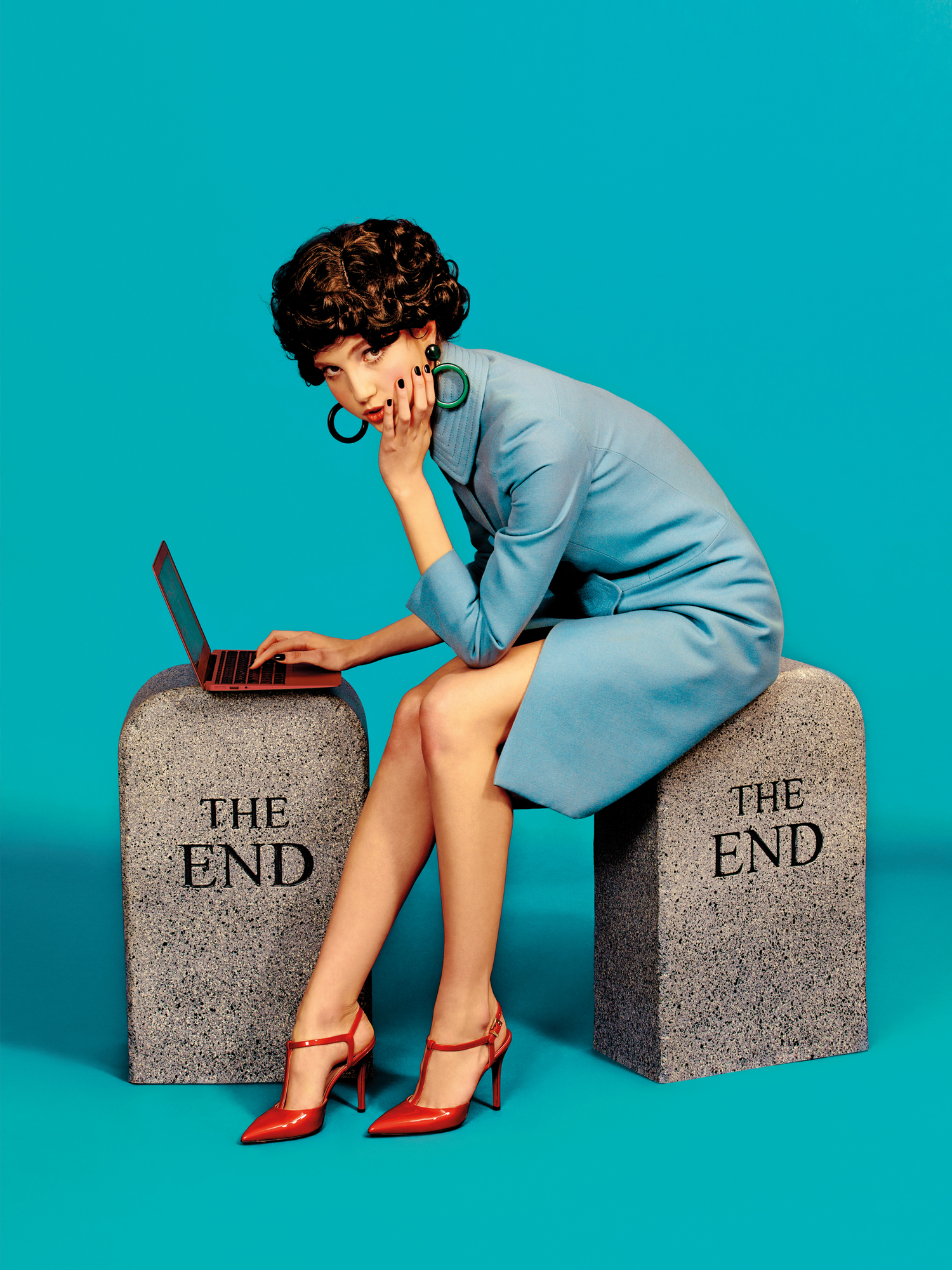 Frau sitzt auf zwei grauen "The End" Hockern von Gufram und tippt auf einem Laptop.