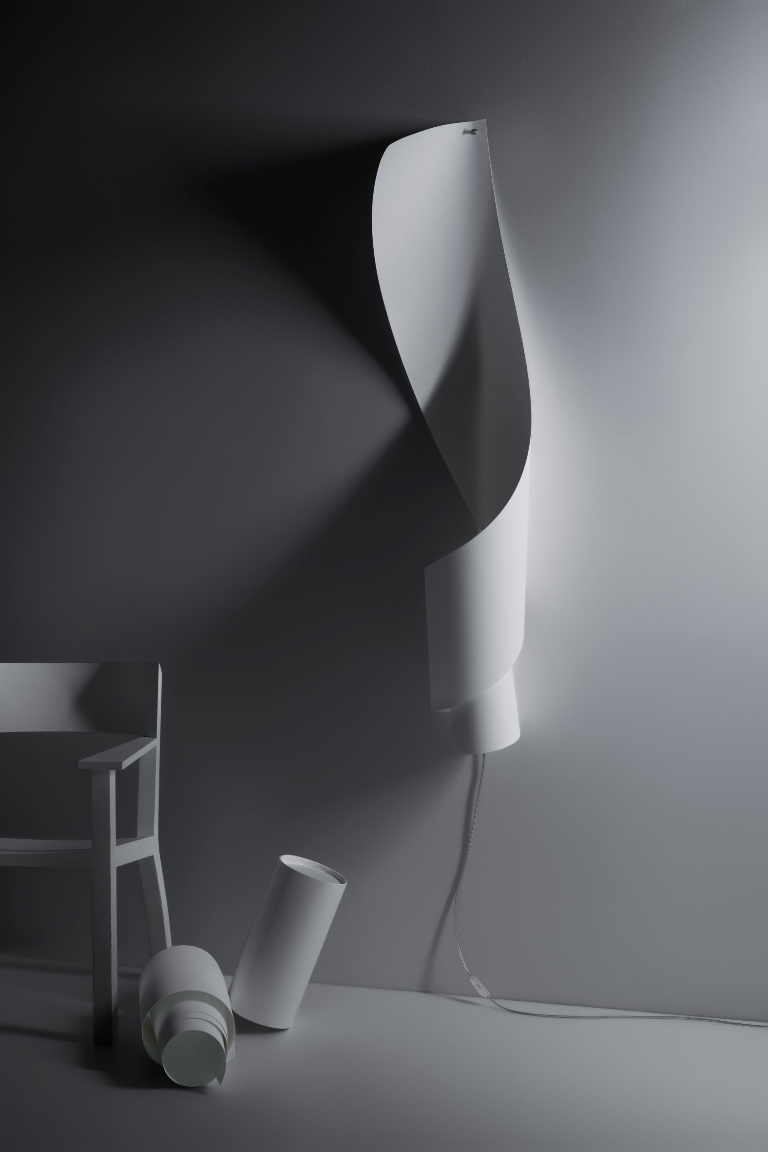 Oop´s Wandleuchte von Ingo Maurer: Geschwungene, weiße Designlampe an der Wand, daneben ein Stuhl.