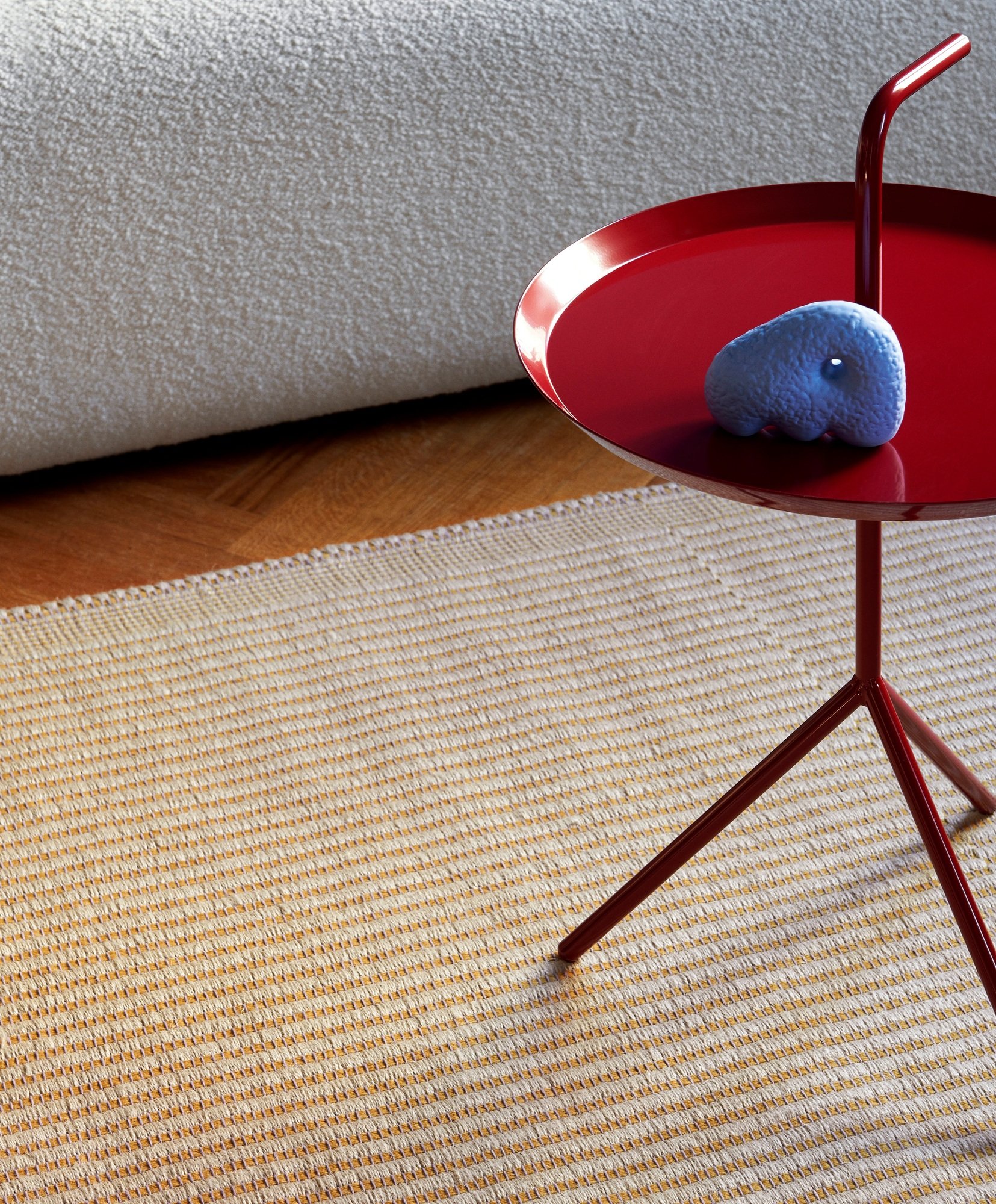 Detailaufnahme des Hay Tapis Teppichs in Beige und Orange mit rotem Beistelltisch und Dekoration.