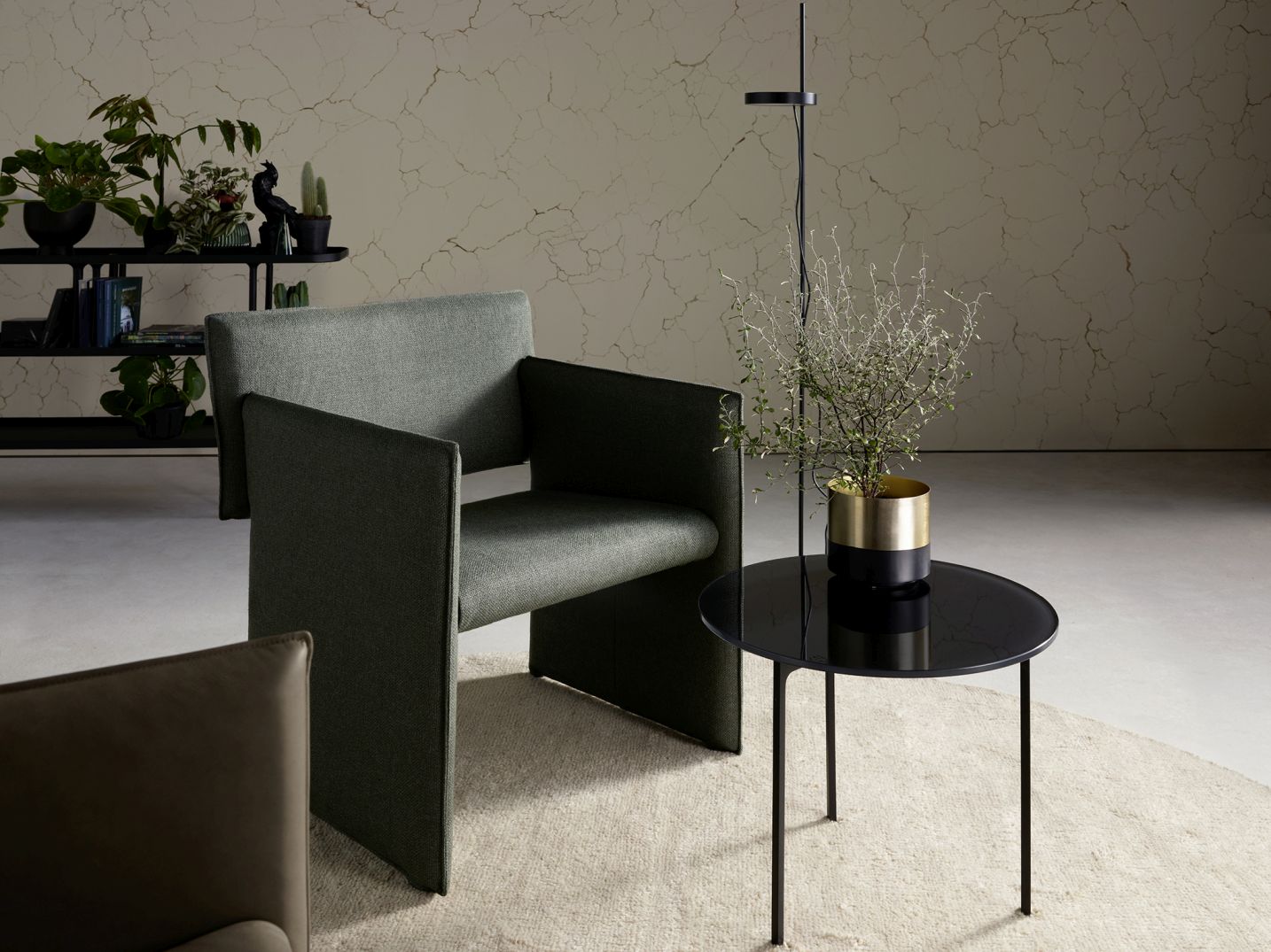 Noto Sessel mit Wangen von Cor in grünem Stoffbezug neben einem schwarzen Beistelltisch.