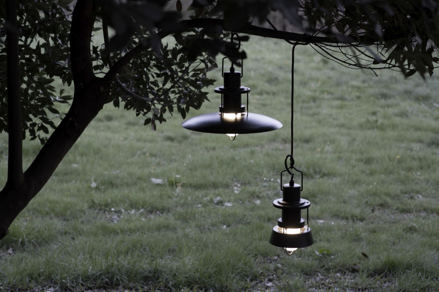 Zwei schwarze Martinelli Luce Outdoor Pendelleuchten hängen an einem Baum im Garten.