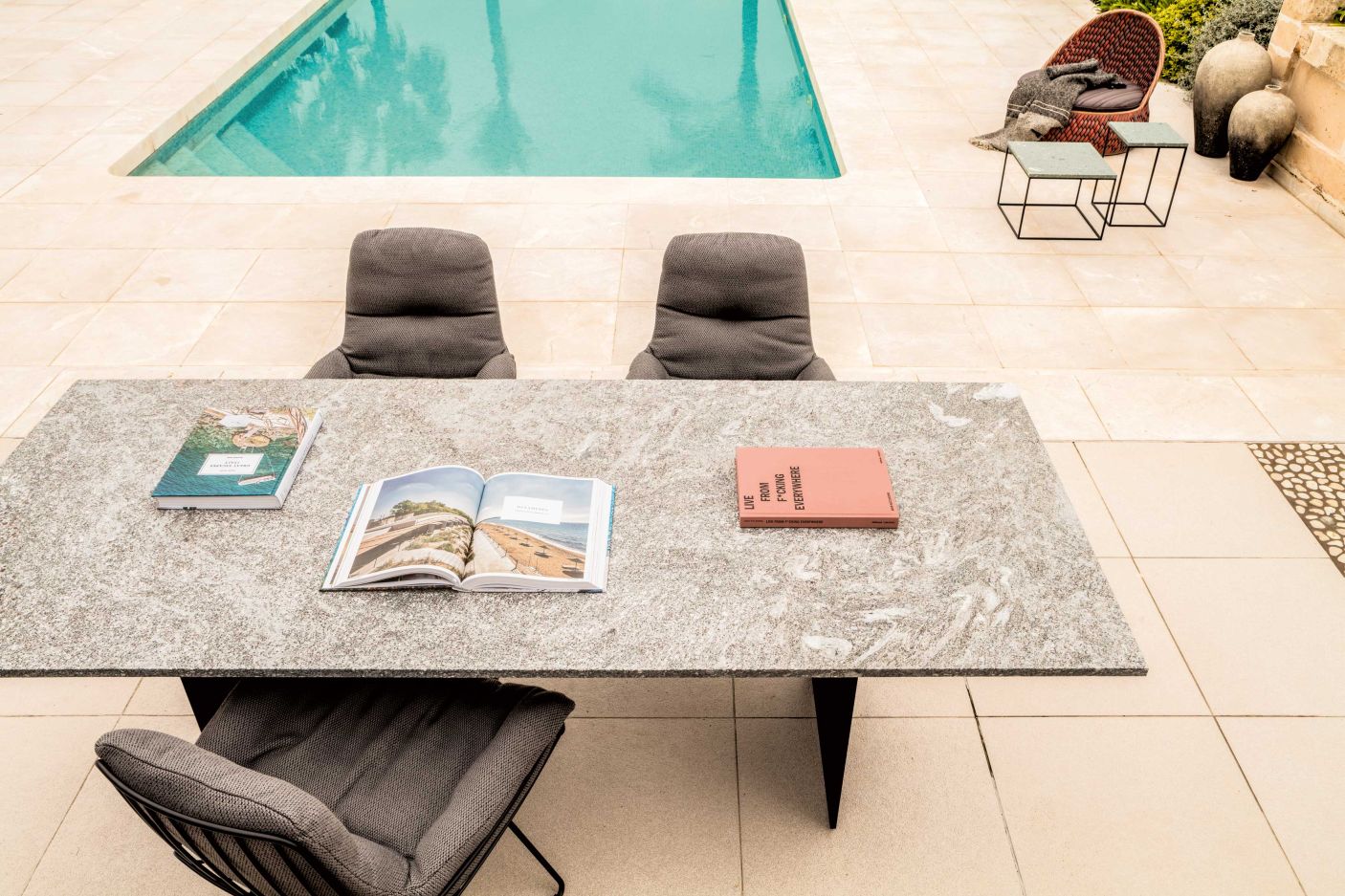 SC 41 Outdoor Tisch Stein Alps Glitter von Janua mit Stühlen und Büchern am Pool.