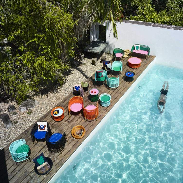 Ames Caribe Esstisch Outdoor und farbenfrohe Gartenmöbel am Pool, Person schwimmt.