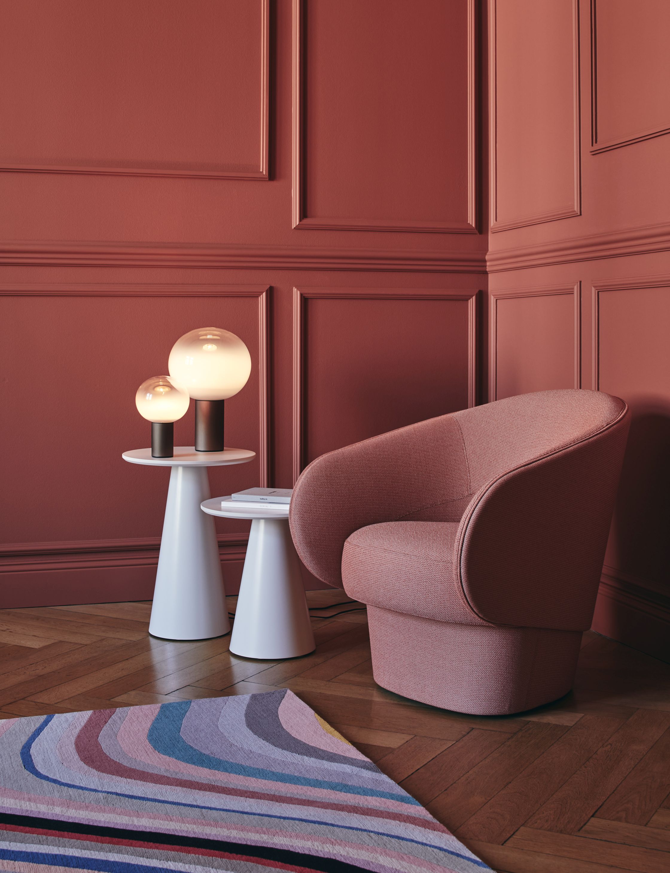 Laguna Tischleuchte von Artemide in Bronze auf weißem Beistelltisch, neben Sessel.