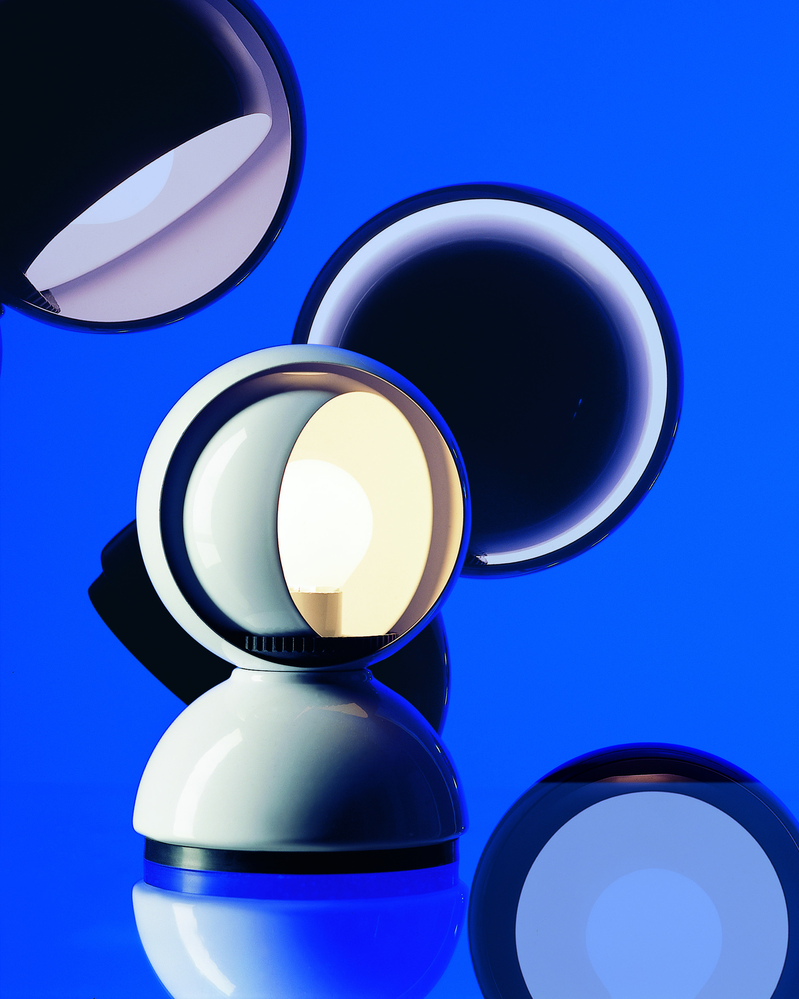 Weiße Artemide Eclisse Tischleuchte mit verstellbarem Schirm und warmem Licht auf blauem Hintergrund.