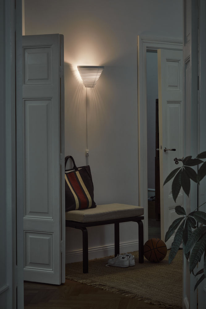 Artek A910 Wandleuchte in einem Flur, neben einer Bank mit Tasche und Schuhen.