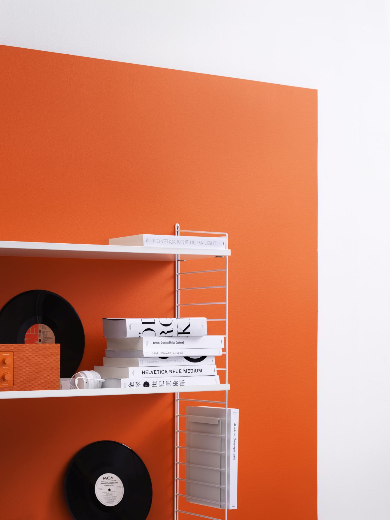 Weißes String Regalsystem an oranger Wand mit Schallplatten und Büchern. Wohnzimmer Regale.
