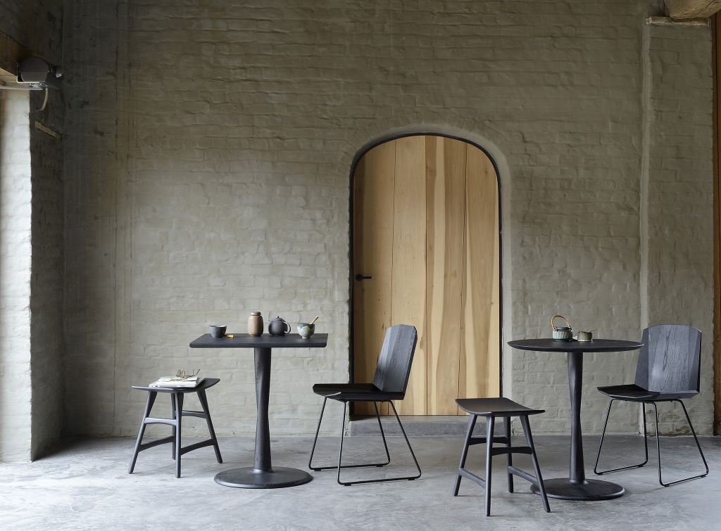 Ethnicraft Torsion Eiche Esstisch B 70 schwarz mit passenden Stühlen und Hockern vor Backsteinwand.