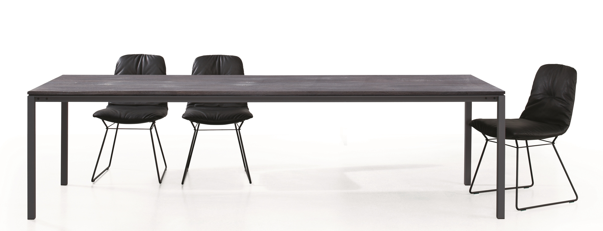 S 600 Tisch von Janua: Esstisch aus geköhlter Eiche mit schwarzen Stühlen auf weißem Hintergrund.