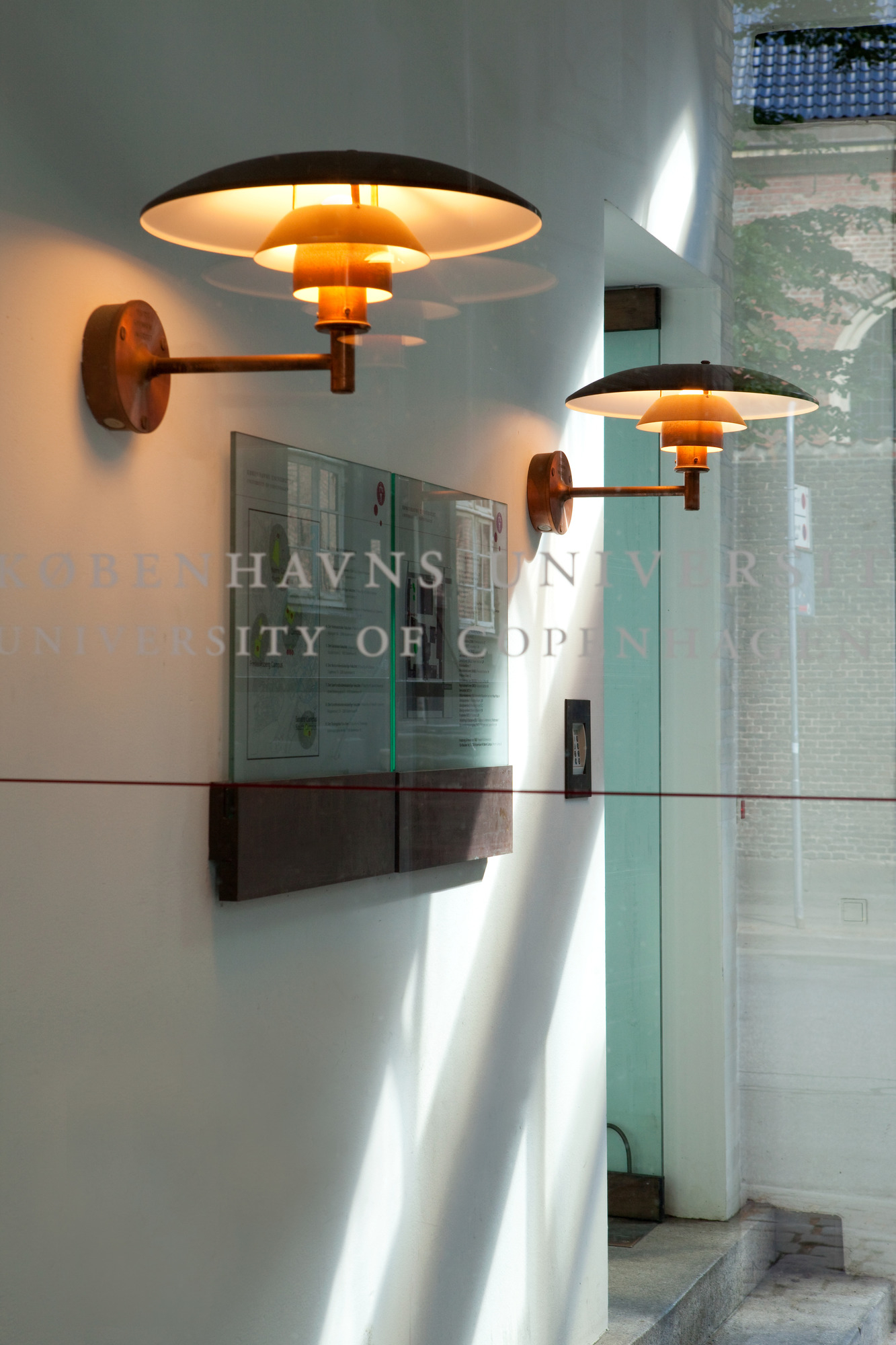 Zwei PH Wall Outdoor Wandleuchten von Louis Poulsen spenden warmes Licht an einer Fassade.