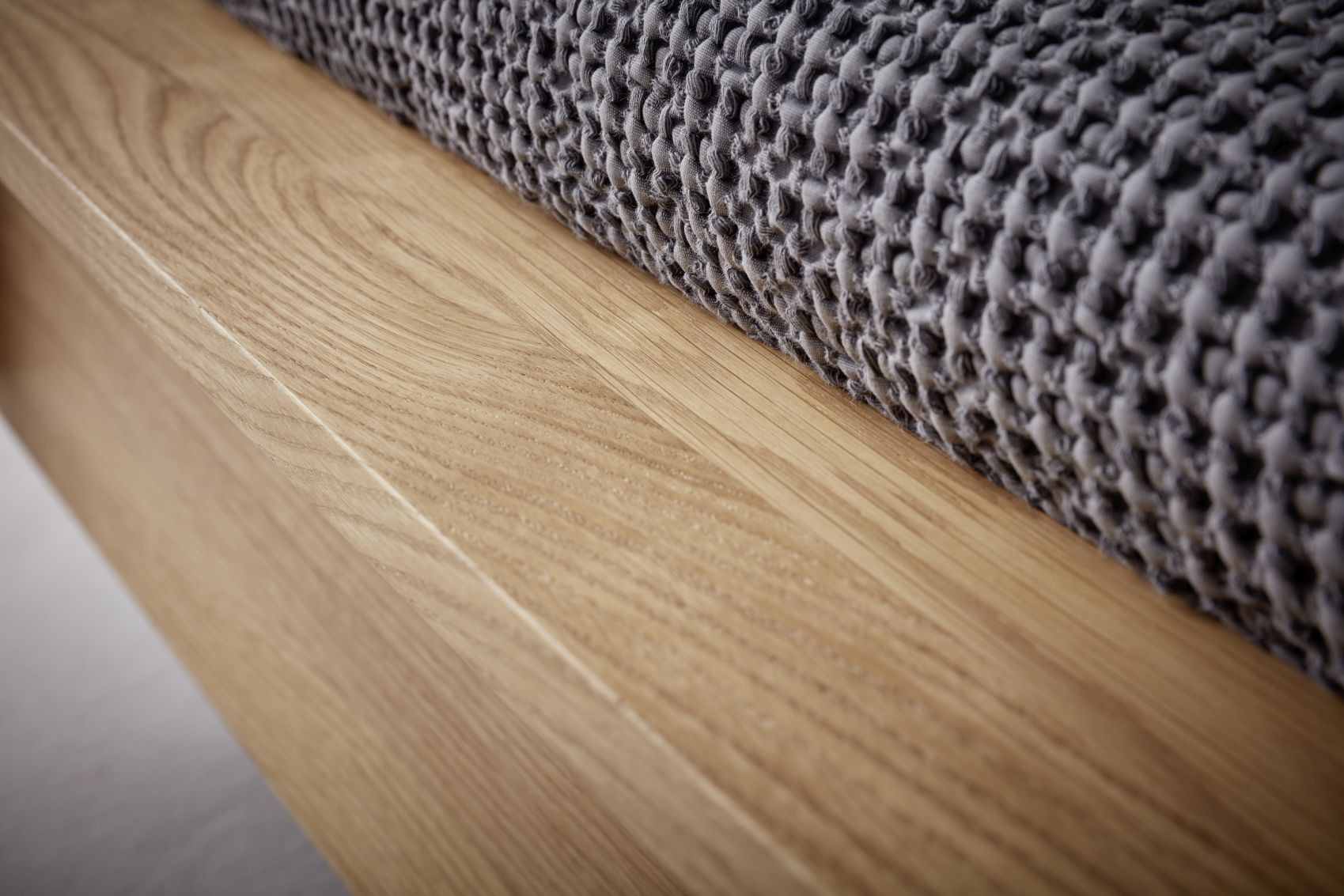 Detailaufnahme: Flai Doppelbett Eiche von Müller Möbelwerkstätten mit grauer Tagesdecke. Massivholz Bettrahmen mit natürlicher Holzmaserung.
