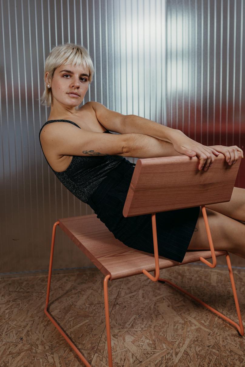 Frau sitzt auf D:007 Loungechair von Fuchs & Habicht. Design Stuhl mit Holz und orangefarbenem Gestell.