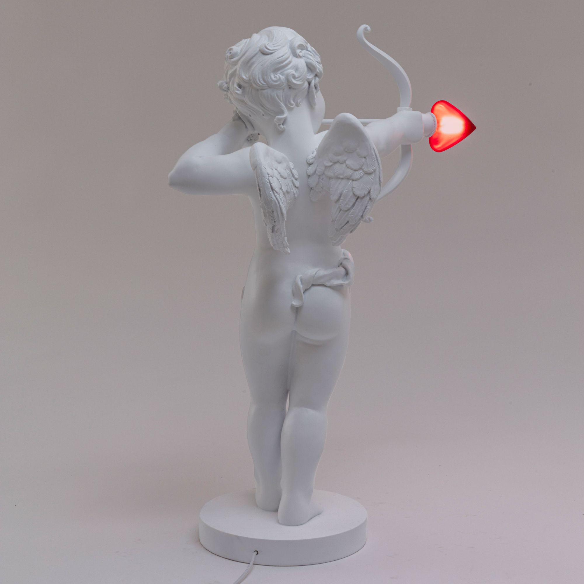 Rückansicht der weißen Seletti Cupid Lampe mit leuchtendem Herz-Pfeil. Tischleuchte für Valentinstag.