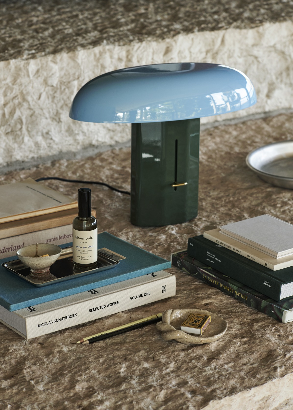 Montera Tischleuchte von AndTradition, blau-grüne Designerlampe auf Büchern, modernes Wohnaccessoire für stilvolle Beleuchtung.