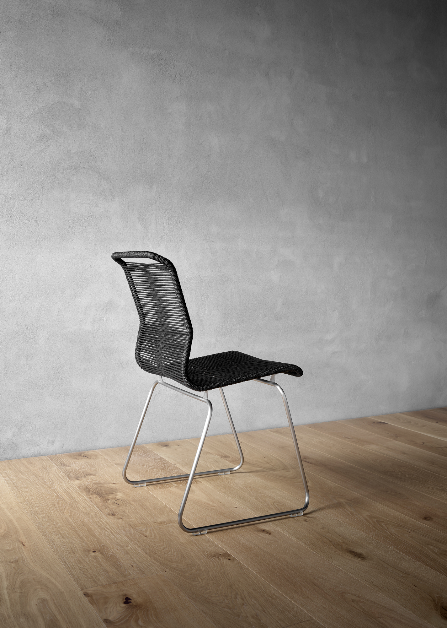 Panton One Outdoor Stuhl in Schwarz mit Edelstahlgestell auf Holzboden vor grauer Wand.