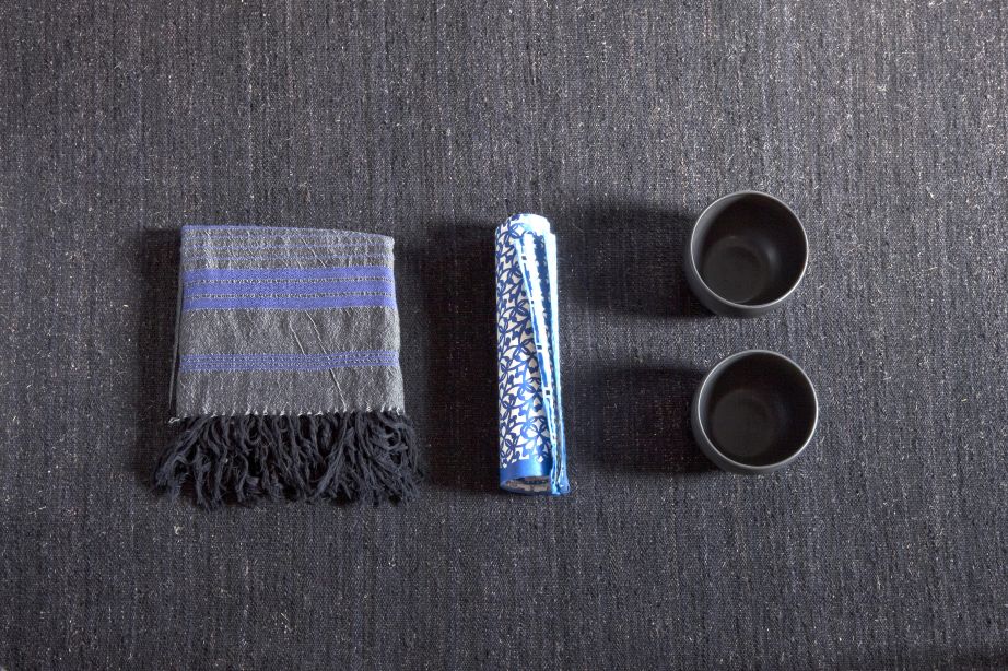 Detailaufnahme des grauen Nomad Teppichs von Nanimarquina mit Fransen, Rolle und zwei Tassen.