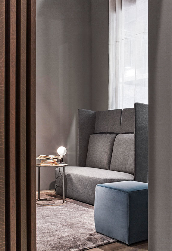 Weiße Flos Lampadina LED Tischleuchte auf Beistelltisch neben grauer Couch und blauem Hocker.