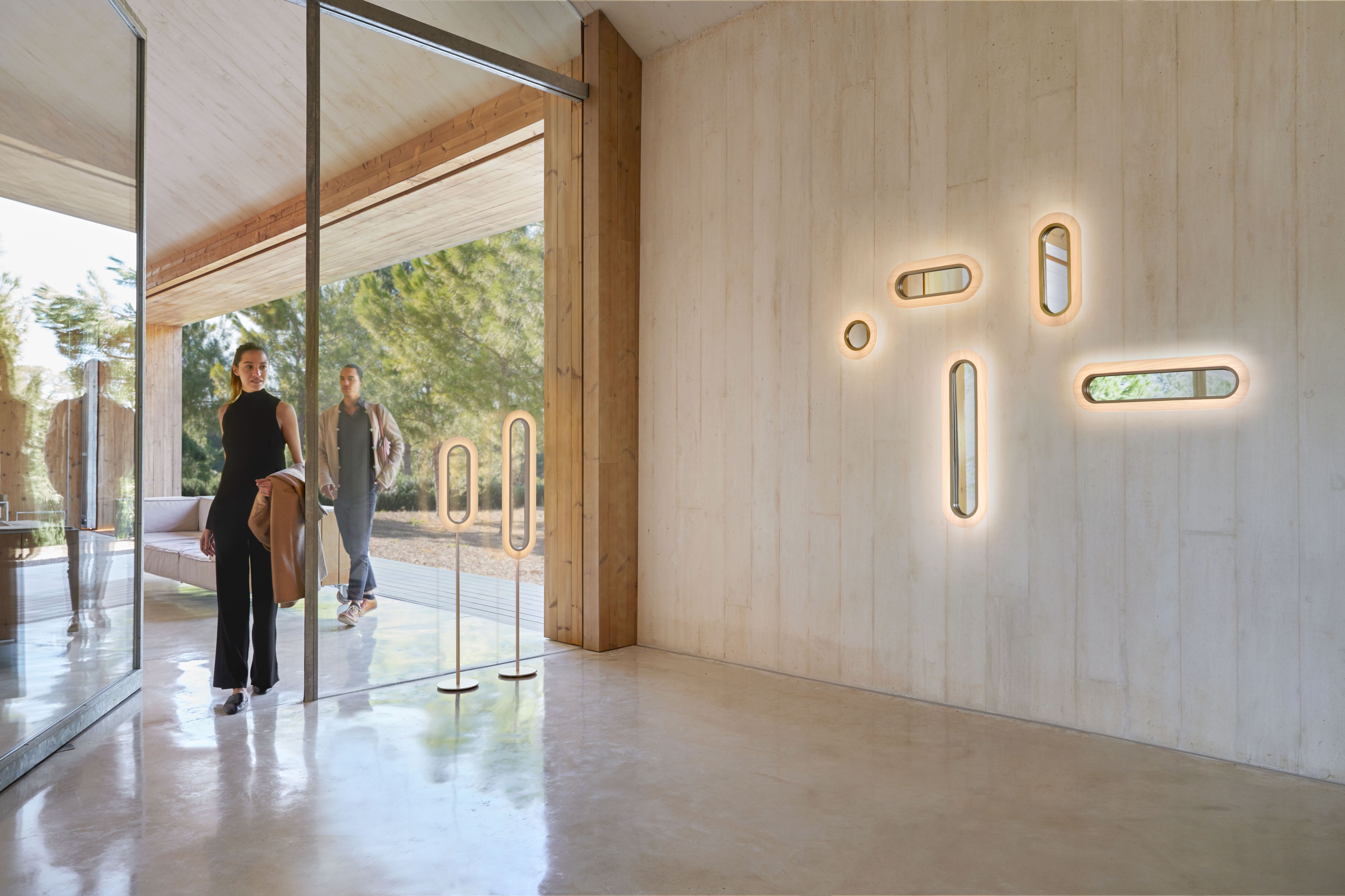 Lens LED Wandleuchten von LZF Lamps: Ovale, hellrosa Leuchten mit goldenem Metallring an einer Wand.