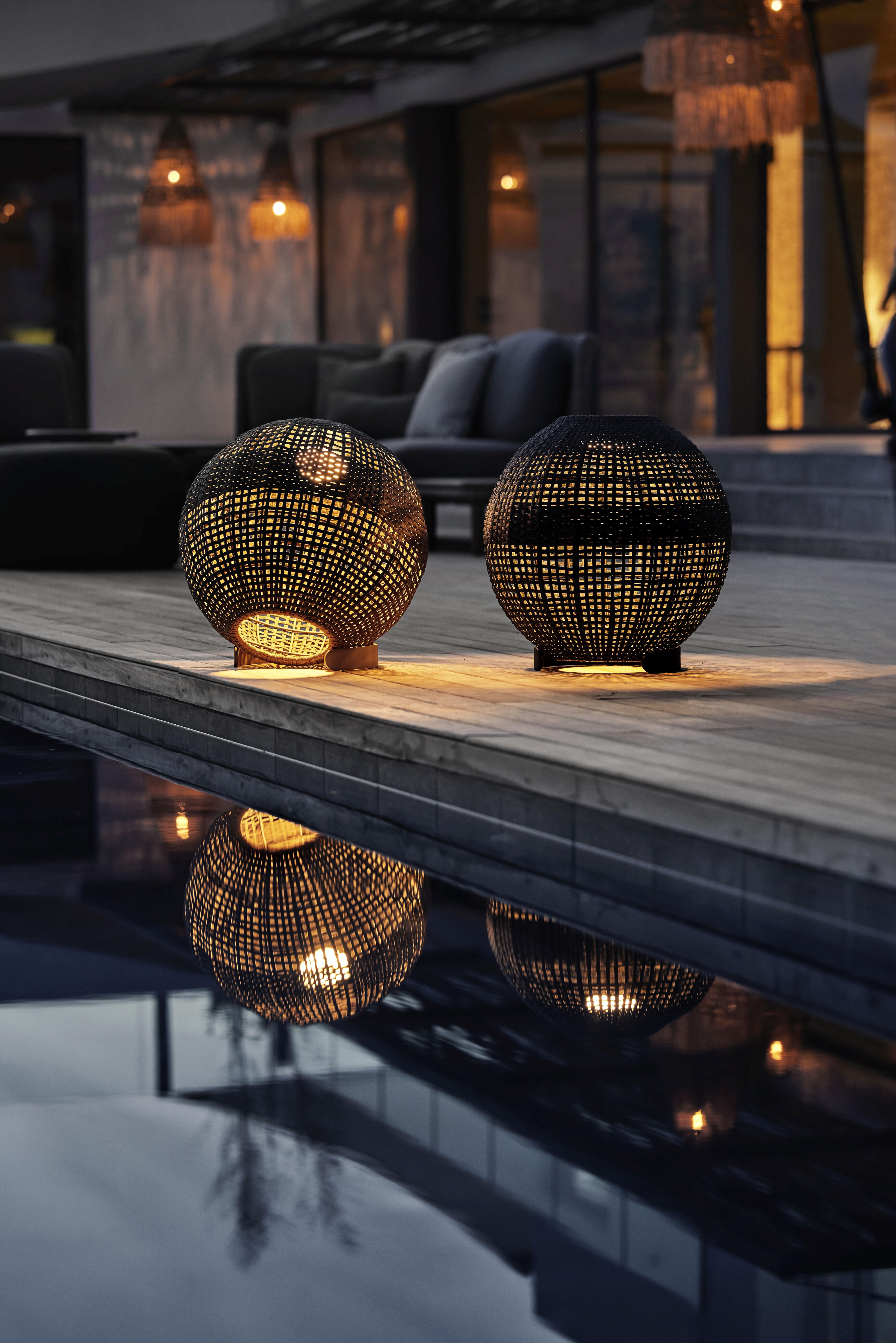 Zwei runde Cane-Line Outdoor Lampen in Dunkelgrau, beleuchtet, mit Reflexion im Wasser.