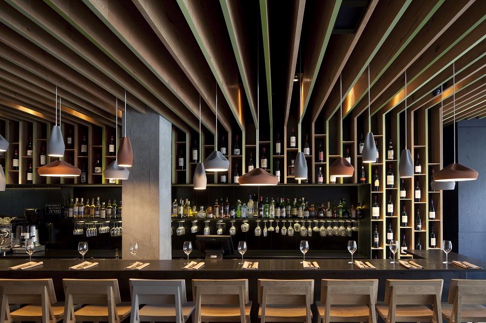 Pleat Box Pendelleuchten von Marset in Grau und Gold über einer Bar mit Spirituosen.