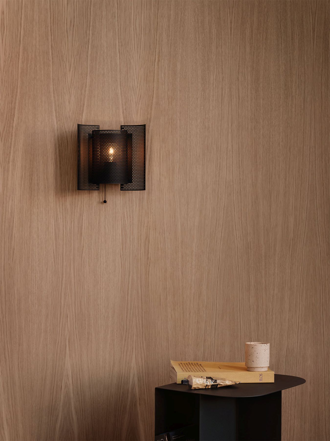 Butterfly Wandleuchte von Northern, gelochtes Metall in Schwarz, warmes Licht an Holzwand.