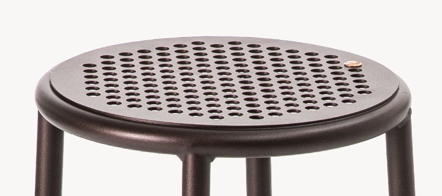 Detailaufnahme: Runder, brauner Nizza Hocker mit gelochter Sitzfläche. Modernes Design für Wohnen und Gewerbe.