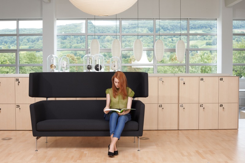 Frau liest auf schwarzem Suita Sofa von Vitra in modernem Büro.