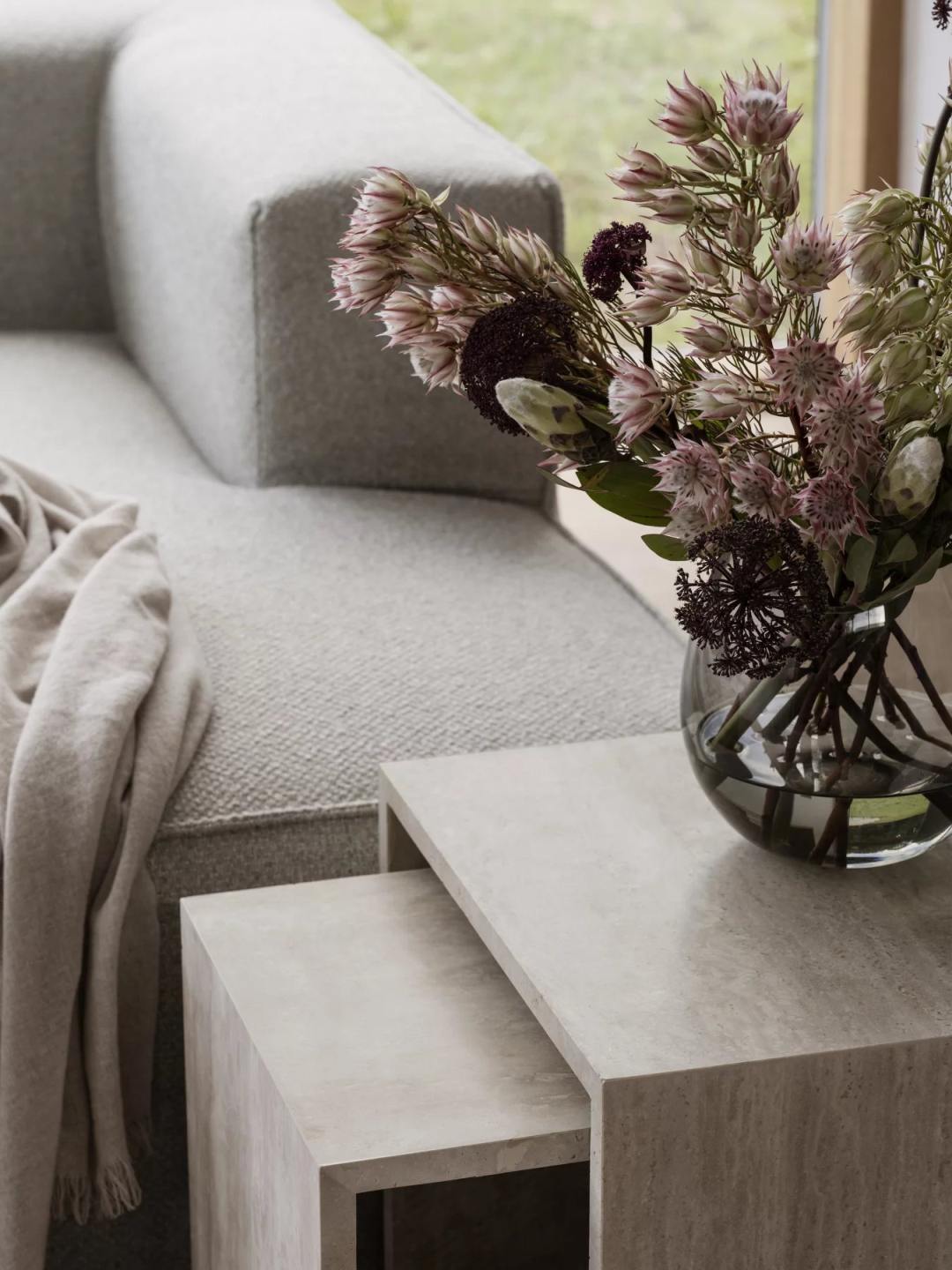 Varu Beistelltisch 2er Set Blomus Tundra Gray neben Sofa mit Blumen in Glasvase.