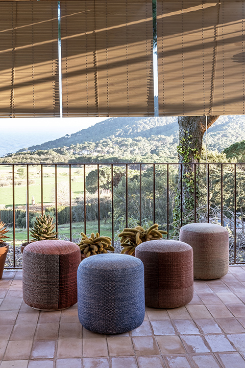 Mehrfarbige Shade Outdoor Pouf Hocker von Nanimarquina auf einer Terrasse mit Ausblick. Sitzhocker für den Garten.
