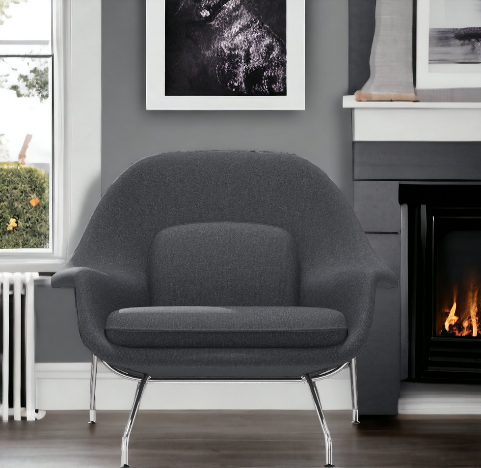 Grauer Womb Chair Sessel von Knoll International mit Chromgestell vor Kamin und Fenster.