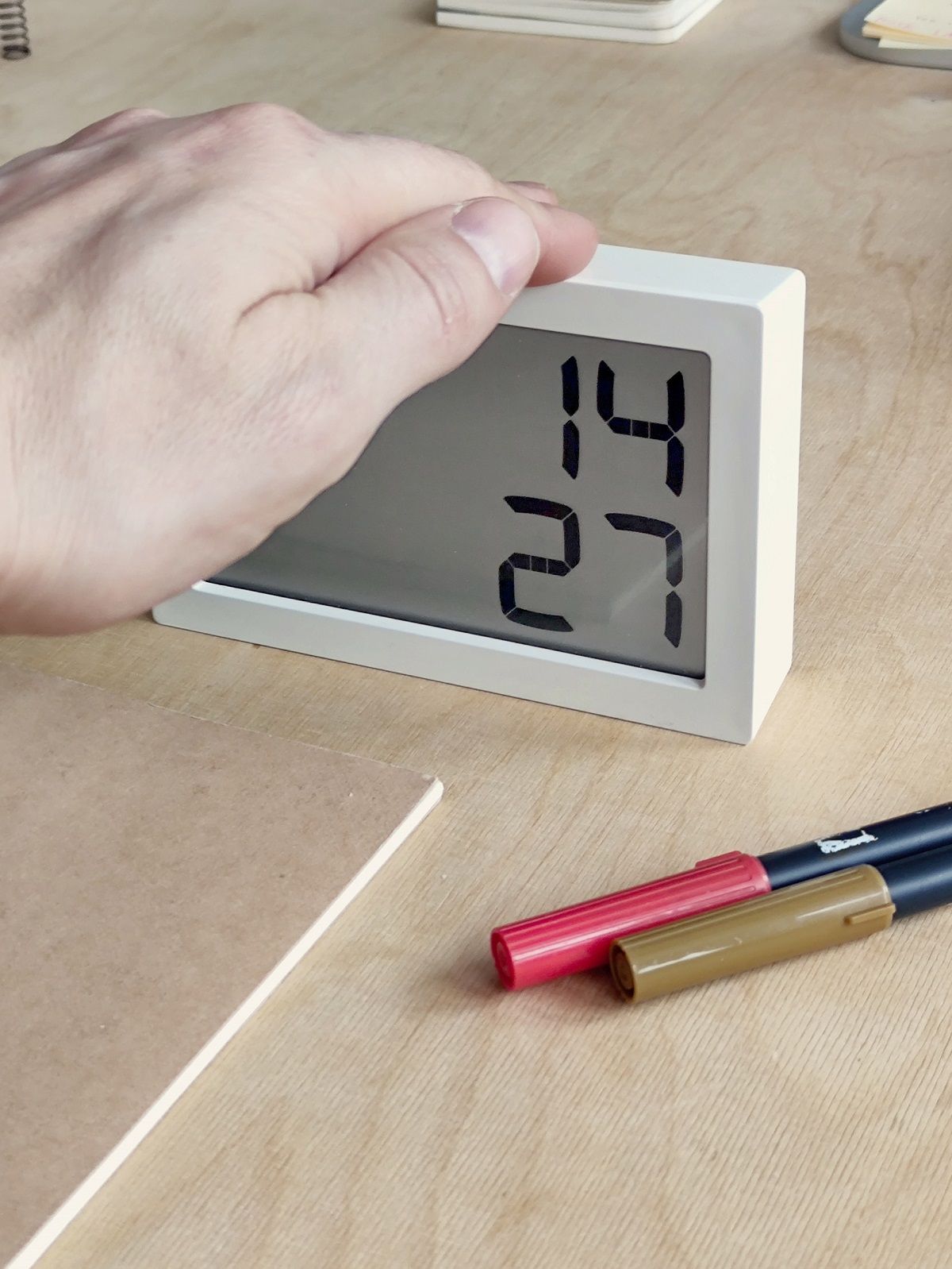 Weiße LED Digitaluhr (Albert Clock) auf einem Schreibtisch, Hand berührt das Display.