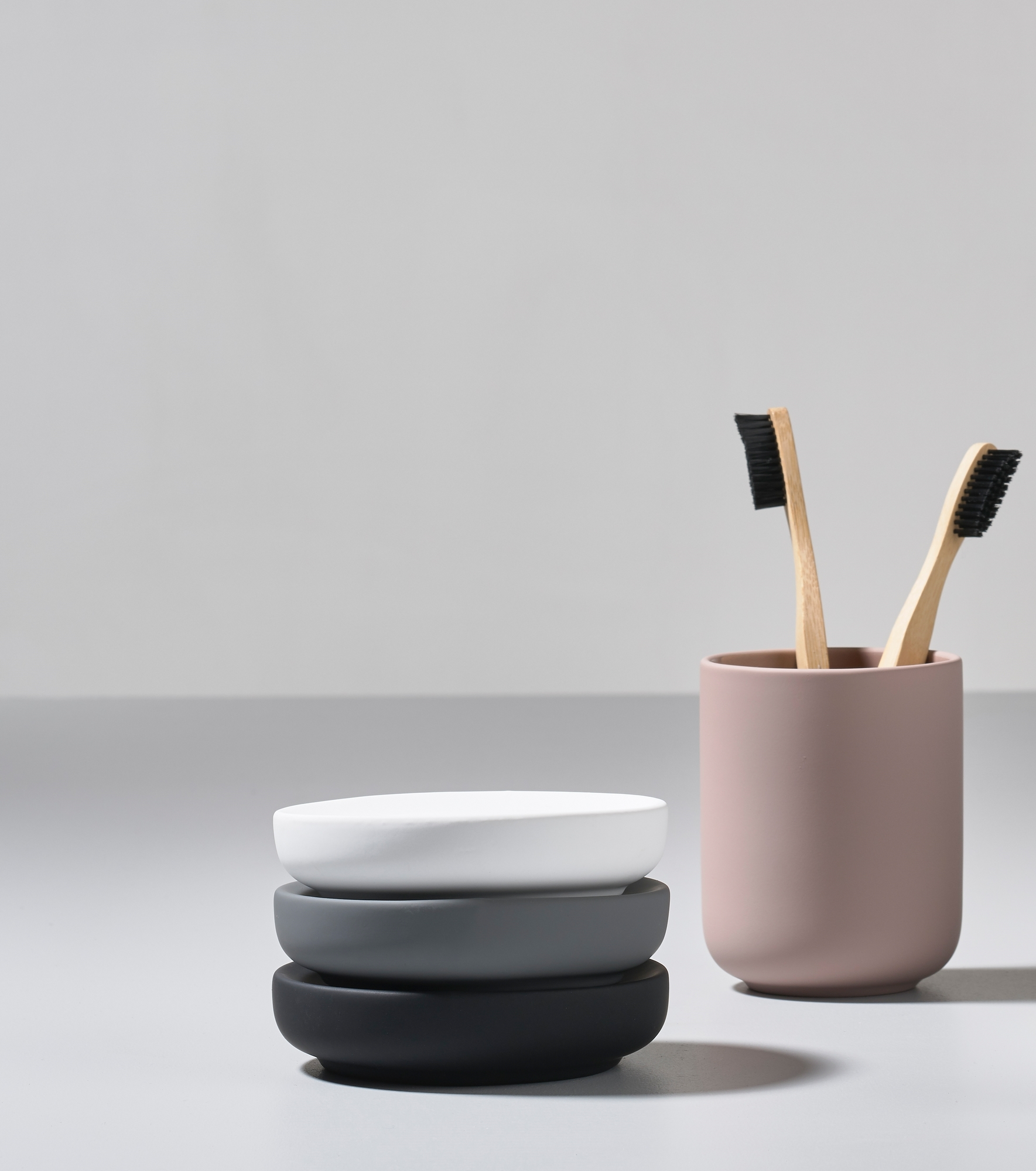Ume Zahnputzbecher von Zone Denmark in Rosa mit Bambus-Zahnbürsten und Seifenablagen in Weiß, Grau und Schwarz.