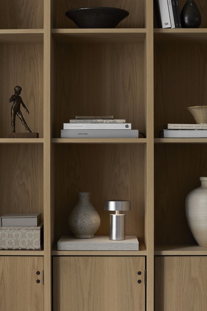 Column Tischleuchte von Audo Copenhagen aus Aluminium auf einem Holzregal mit Deko-Objekten.