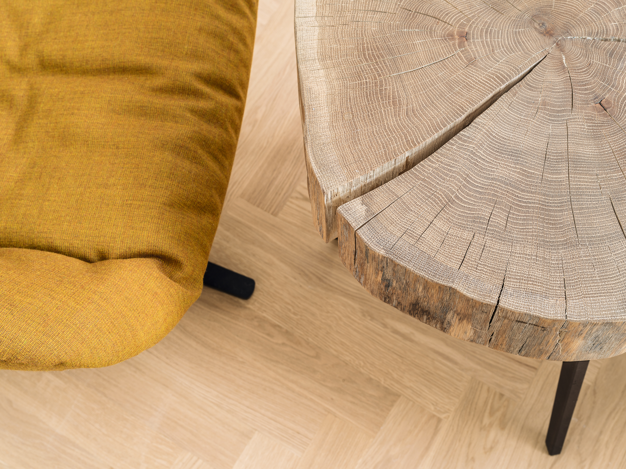 Nahaufnahme des Janua Stomp Beistelltisches H28 aus rohem Holz mit Baumscheiben-Optik neben einem gelben Sessel.