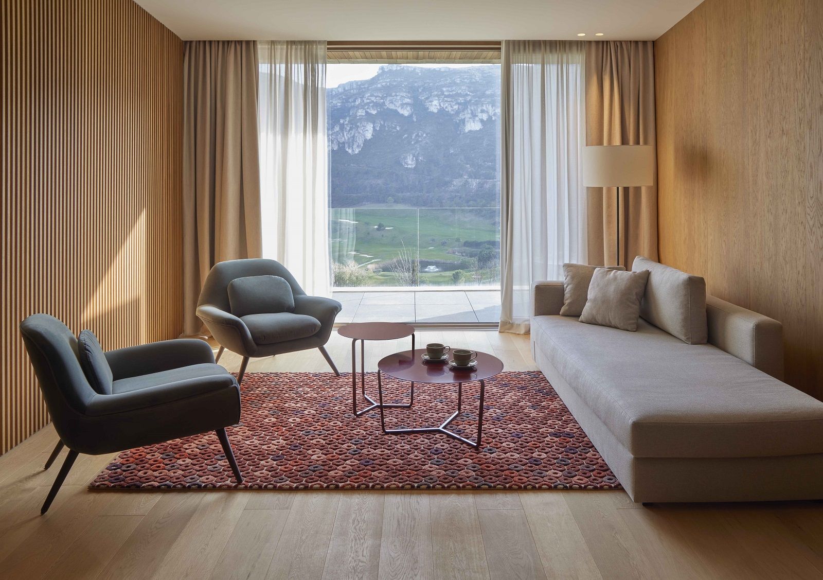 Wohnzimmer mit Chimos Teppich, gemustert, in warmen Farben, vor Sofa und Sesseln.