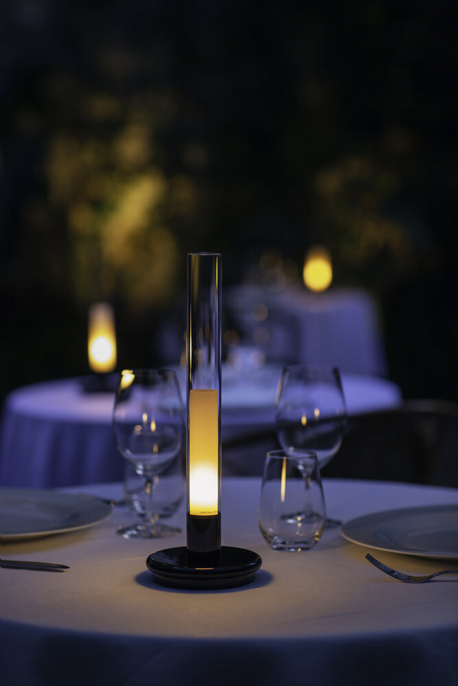 Sylvestrina Tischleuchte von Santa Cole auf gedecktem Tisch, warmes, stimmungsvolles Licht.