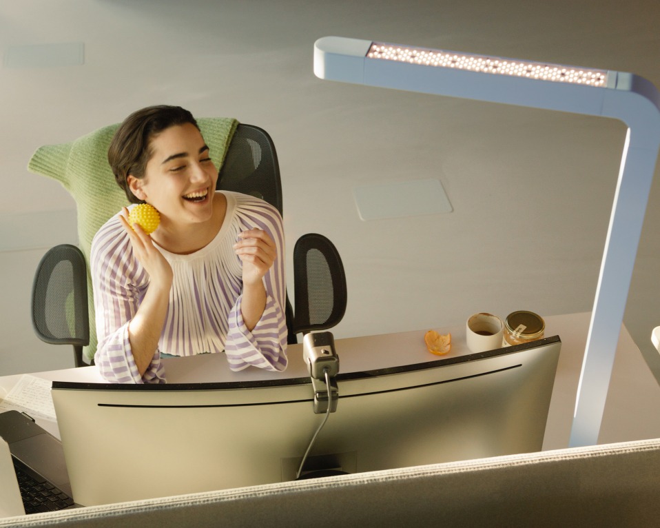 Frau lächelt unter dem Licht der grauen Team Home LED Tischleuchte am Schreibtisch.